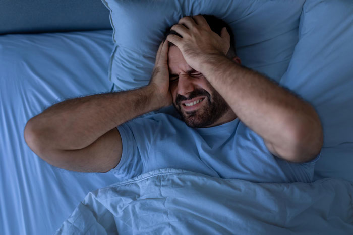 Man in bed holding his head in distress, overwhelmed by the challenges of caring for disabled brother. Man in bed holding his head in distress, overwhelmed by the challenges of caring for disabled brother.