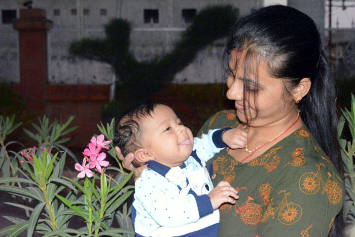 Indian grandmother holding baby, concerned about baby's pale skin, questioning DNA and parentage outside near plants.