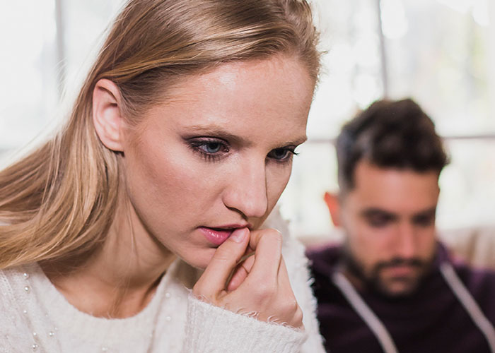 Worried woman thinking deeply while man sits in background, illustrating a master&rsquo;s degree lie and truth discovery.