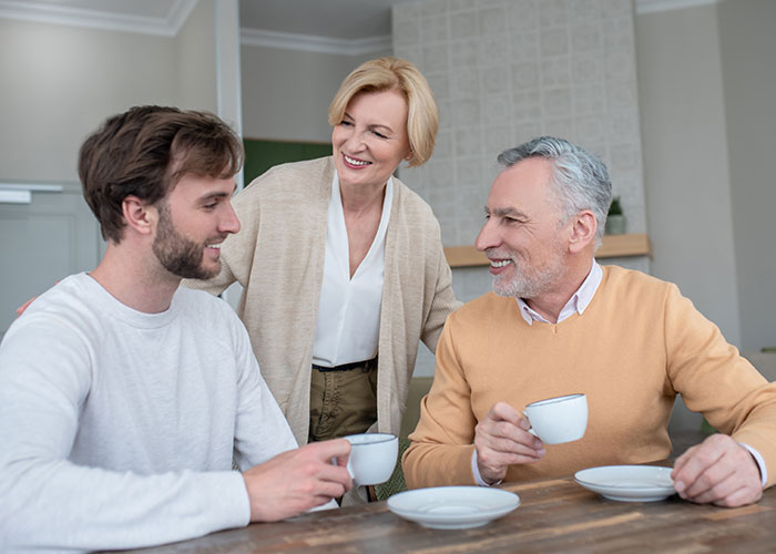 Middle-aged couple and young man having a conversation over coffee, illustrating a story about a master&rsquo;s degree lie.