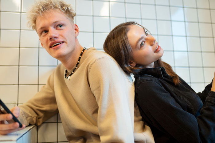 Young man and woman sitting back to back indoors, reflecting on husband retirement and children finances planning.