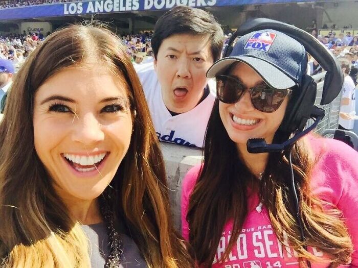 Three people smiling at a Dodgers game with a man photobombing in the background, capturing epic photobombs and laughs.