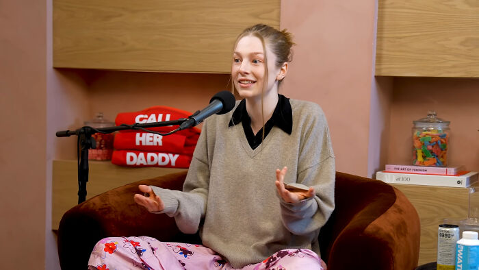 Young woman sitting in a podcast chair speaking into a microphone, sharing James Franco smells stories in a casual setting.