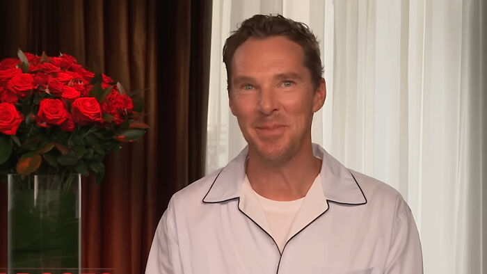 Actor James Franco smiling warmly in a casual white shirt with a bouquet of red roses in the background.