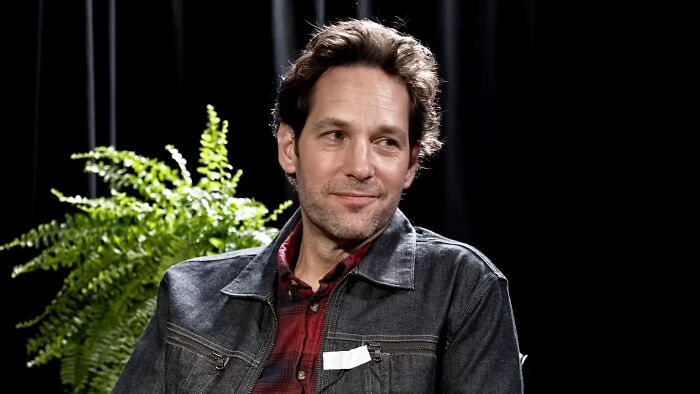 James Franco sitting in a casual setting with a slight smile, wearing a jean jacket and red plaid shirt.
