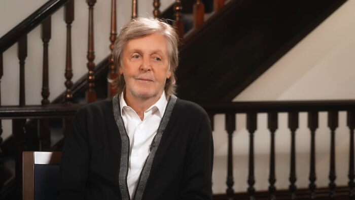 Older man with grey hair and black cardigan sitting indoors near wooden staircase, discussing stories about meeting James Franco.