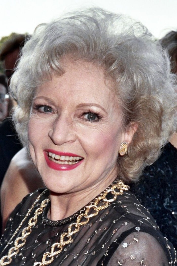 Older woman with curly gray hair and red lipstick smiling at event, representing Hollywood stars who found fame after 30.