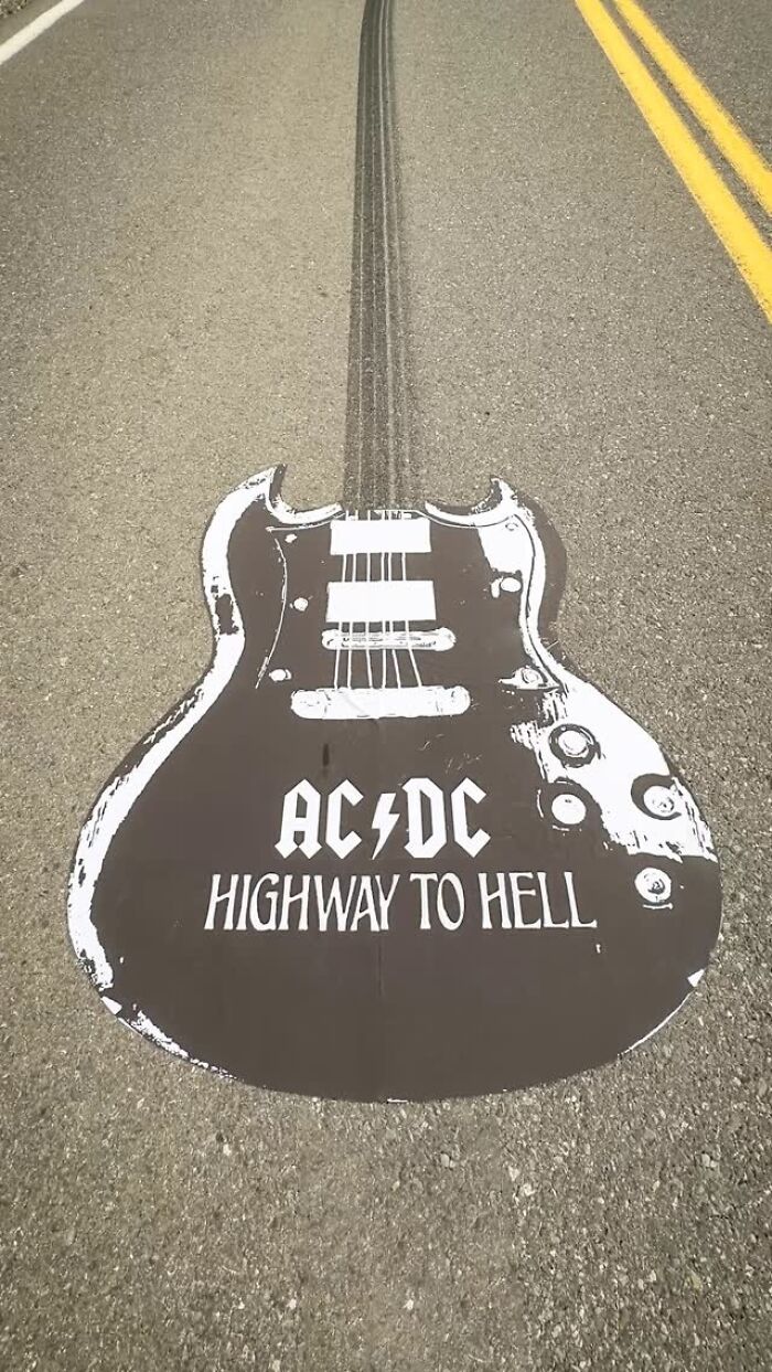 Black and white paper cutout of a guitar with AC/DC highway to hell design on an asphalt road surface