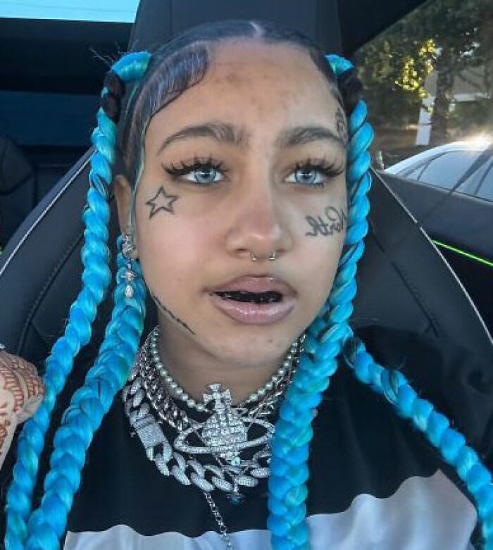 Young person with blue braided hair and face tattoos in car, highlighting celebrity parenting and kids born into fame debate.