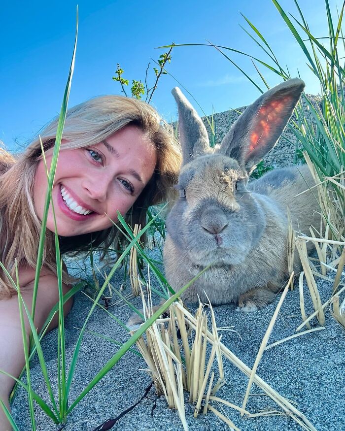 Young woman smiling next to Hoppy Gilmore the rabbit outdoors, showing his affectionate and dog-like companion nature.