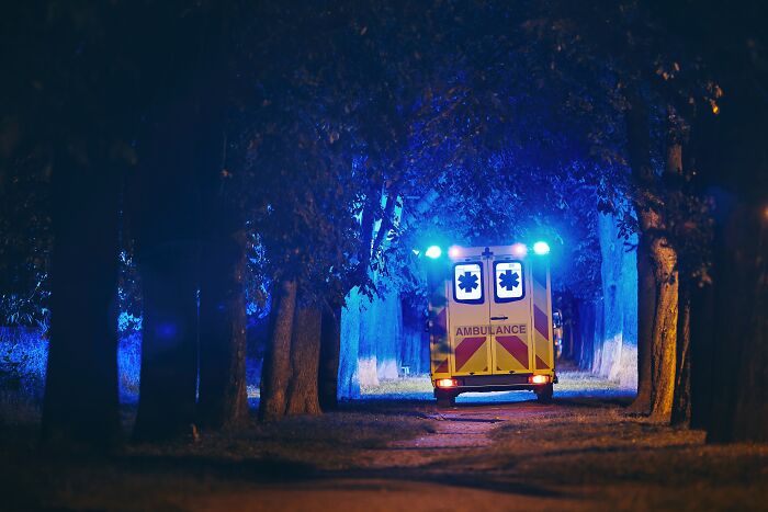 Ambulance with flashing blue lights driving through a dark tree-lined road during a real-life horror story incident.
