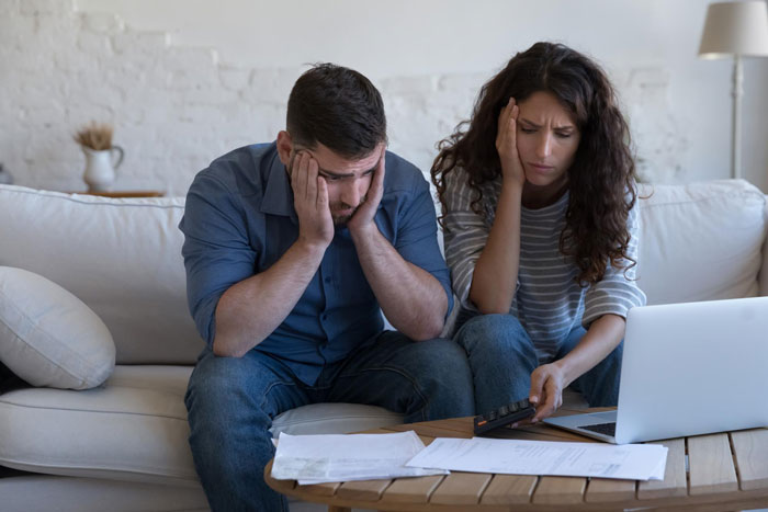 Entitled siblings looking stressed and upset while reviewing papers and using a calculator on a living room couch.