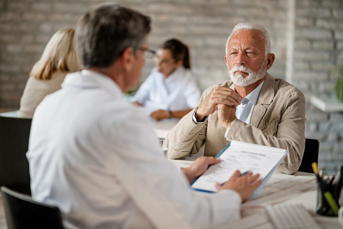 Elderly man consulting a professional, showing concern after learning about being cut from his dad&rsquo;s will and influence issues.