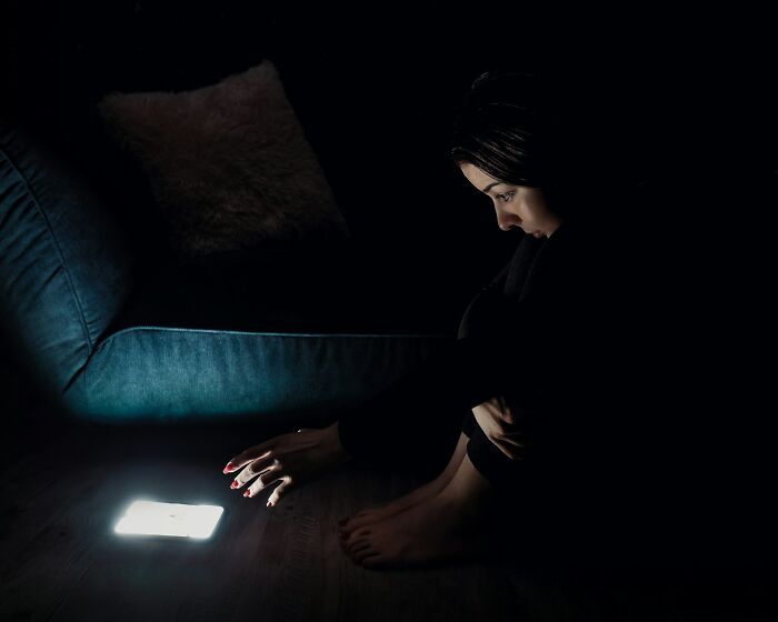 Woman sitting in the dark looking at a phone, illustrating subtle signs that scream they’re cheating in relationships.