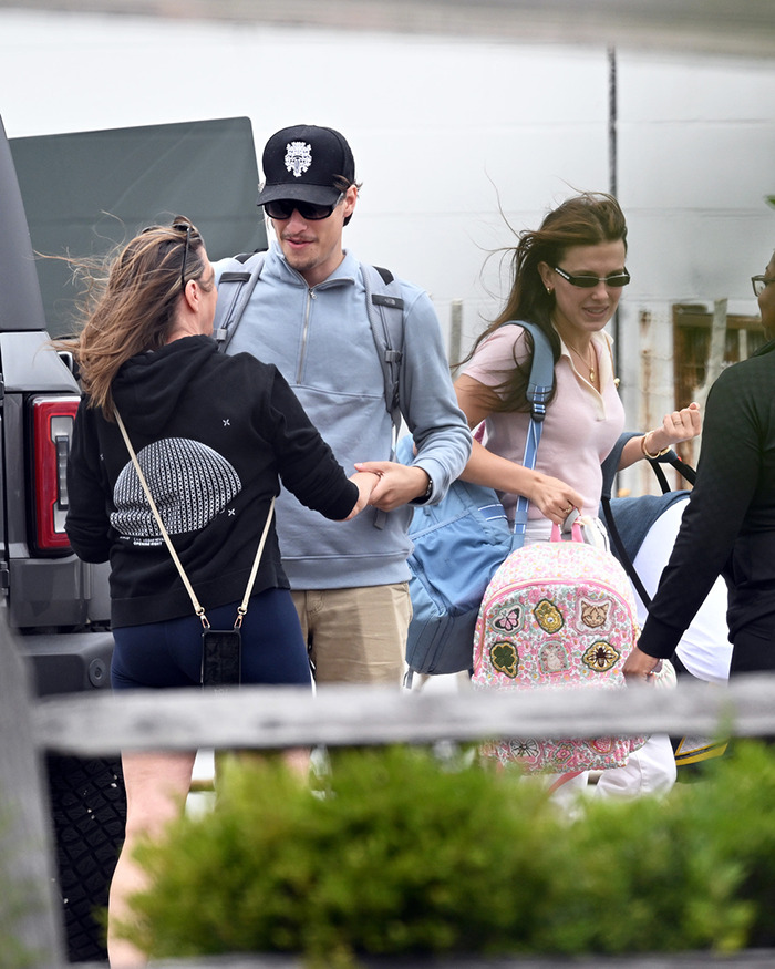 Jake Bongiovi and Millie Bobby Brown walking outdoors, Millie carrying a colorful baby bag with patches and designs.