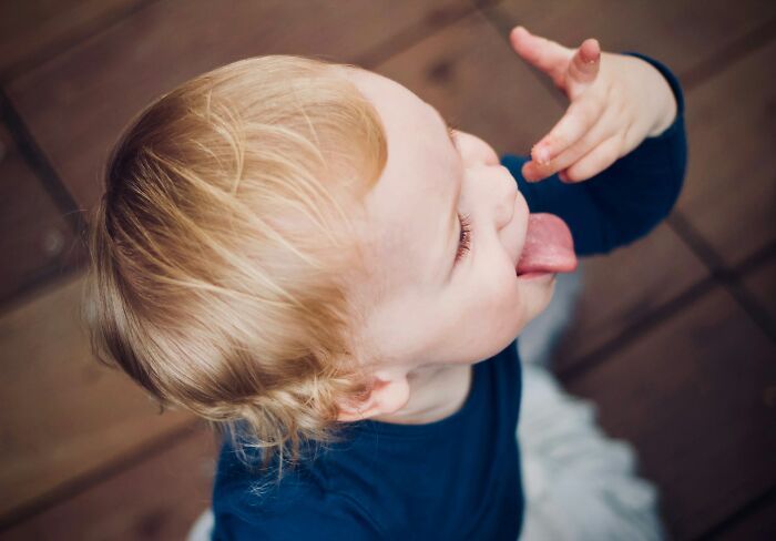 Toddler sticking out tongue and making a funny face, showing weird behavior clearly passed down from their parents.