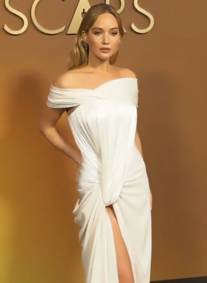 Jennifer Lawrence wearing a white dress resembling a diaper style, sparking plastic surgery speculation at an event.