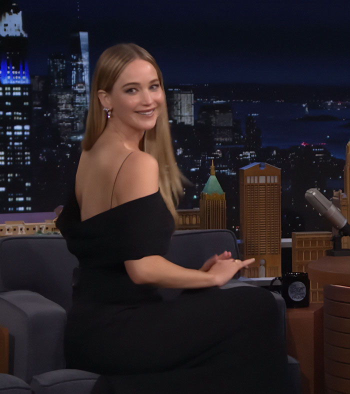 Jennifer Lawrence smiling in a black off-shoulder dress amid increasing plastic surgery speculation.