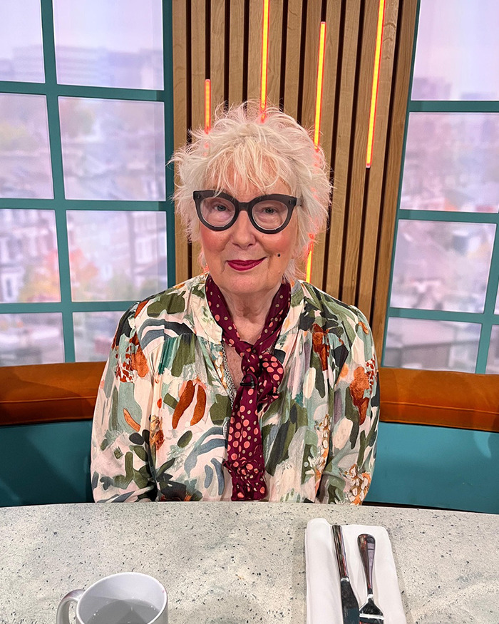 Elderly woman with glasses sitting in a studio setting during a talk show with Nick Offerman X-Rated comment news.