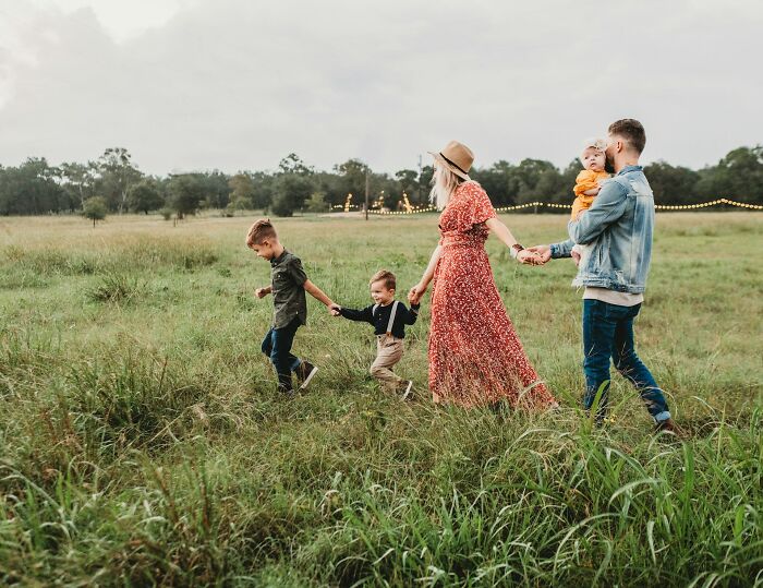 Family walking hand in hand through a grassy field, capturing a uniquely awkward moment in an outdoor setting.