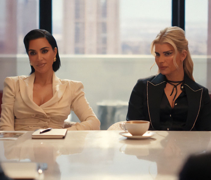 Two women seated at a conference table, highlighting Jessica Simpson's botched plastic surgery in her acting return role.