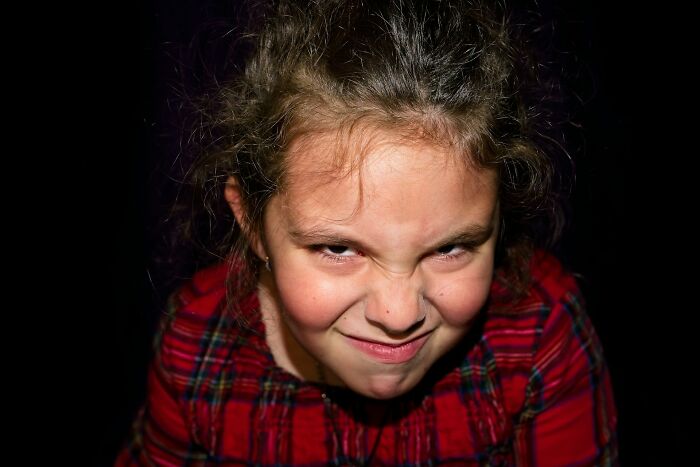 Child making a funny, mischievous face wearing a red plaid shirt showing a quirky behavior passed down from parents.