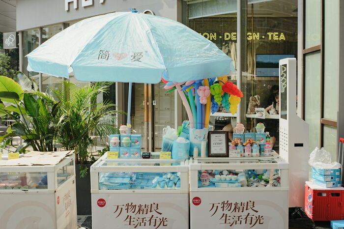 Black Friday chaos at an outdoor shopping stall with colorful balloons and packed product displays under a blue umbrella.