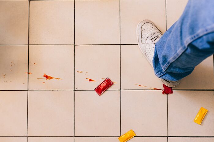 Person in white sneaker stepping on spilled condiments on tiled floor, illustrating worst things seen on Black Friday by employees
