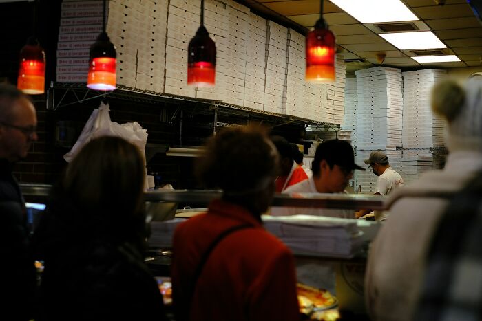 Workers share unprofessional things done in a busy pizza shop kitchen with staff and customers visible.
