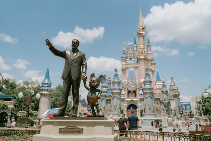 Statue of Walt Disney and Mickey Mouse in front of a castle with tourists, illustrating absurd but true stories.