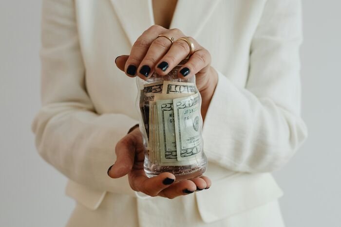 Person in white blazer holding a broken piggy bank with US dollar bills illustrating toxic relationship traits.