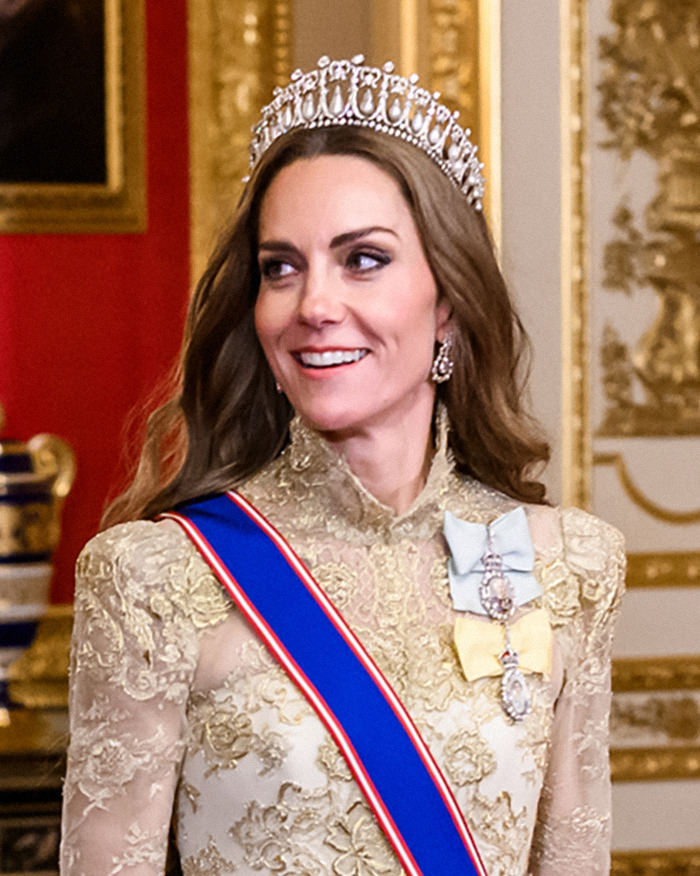 Kate Middleton smiling indoors wearing a tiara and a gold dress, her hair looking unnaturally healthy and blonde.