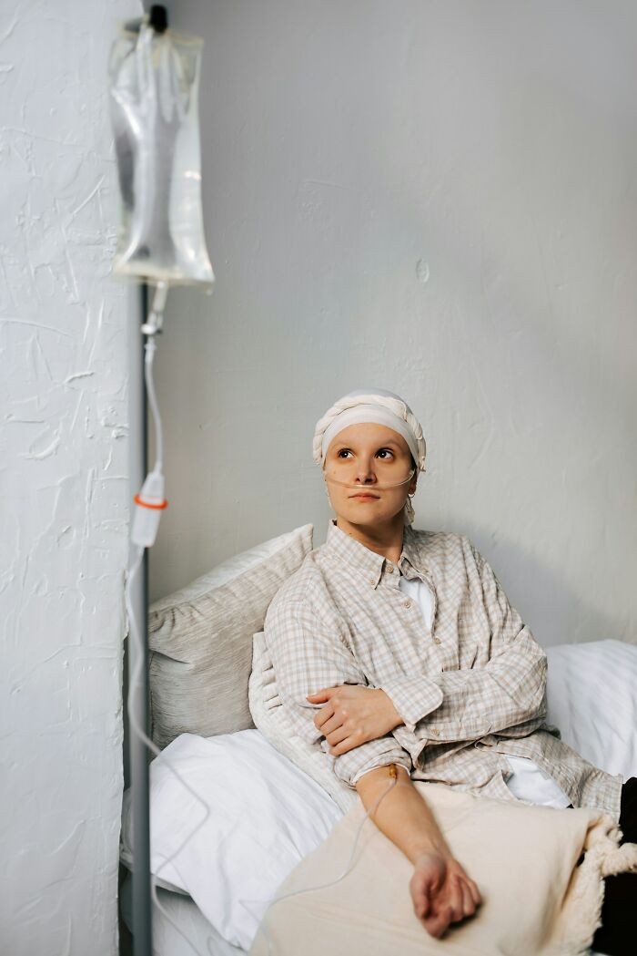 Person undergoing cancer treatment sitting in bed wearing a headscarf with IV drip in a calm clinical setting