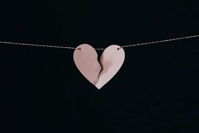 Torn paper heart hanging on string against dark background symbolizing subtle signs of cheating in relationships.