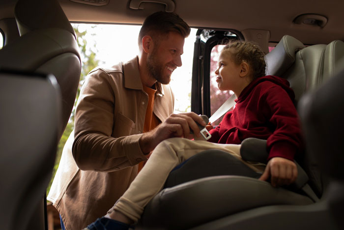 Man helping child in car seat, illustrating family tensions as mom prioritizes widowed friend over kids. Man helping child in car seat, illustrating family tensions as mom prioritizes widowed friend over kids.