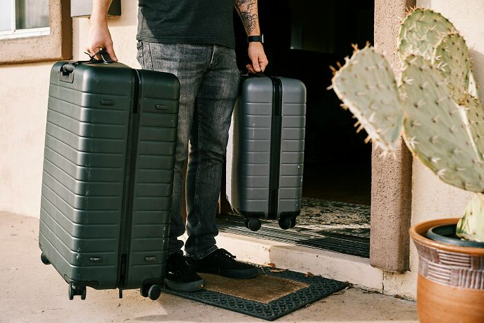 Person standing at doorway holding two large suitcases, depicting refusal to let sister move in after arriving.