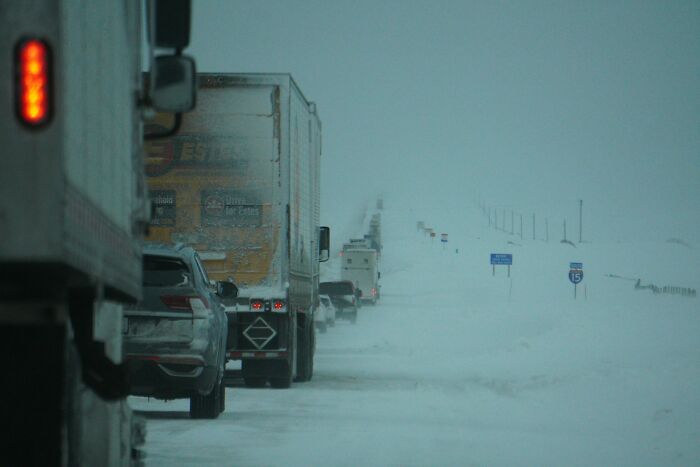 Long line of trucks and cars driving cautiously on a snowy interstate at night, evoking haunting trucker road scenes.