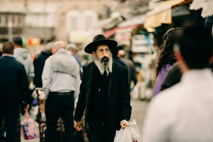 Man with a beard and hat walking through a crowded street market, capturing a moment people wanted to say something funny.