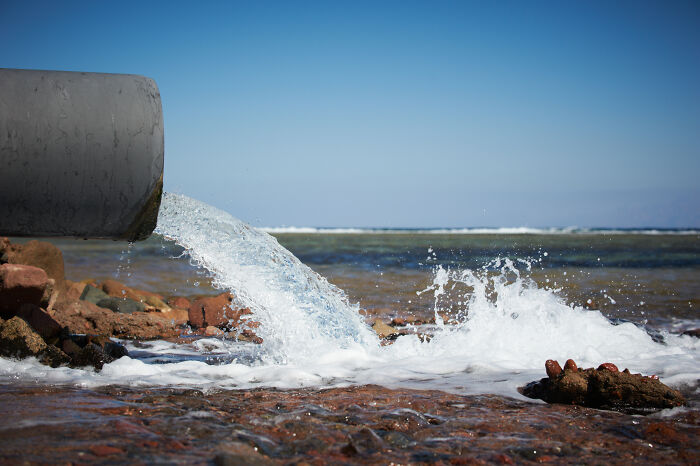 Water flowing from a pipe into a rocky shoreline under a clear sky, illustrating interesting laws and loopholes concept.