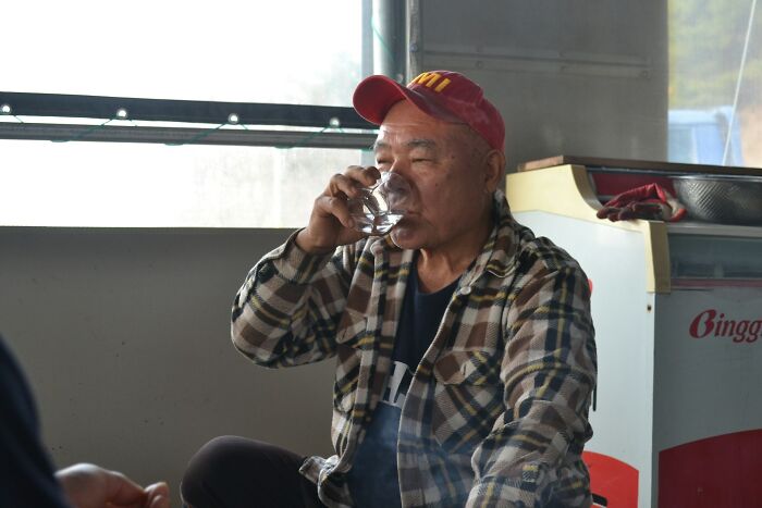 Elderly man in a red cap and plaid shirt drinking water, capturing moments folks wanted to say something funny to loved ones.