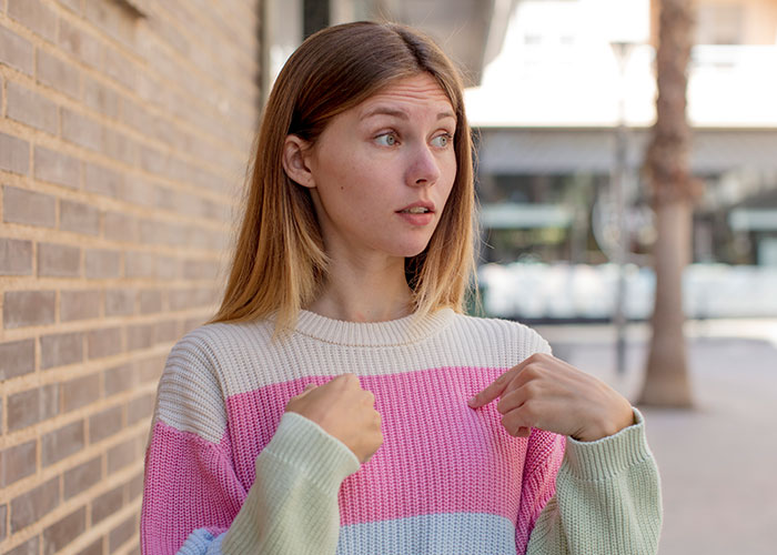 Young woman in colorful sweater pointing at herself, sharing things learned embarrassingly late in life concept.