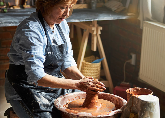 Woman wearing apron shaping clay on pottery wheel, illustrating people learning skills embarrassingly late in life.