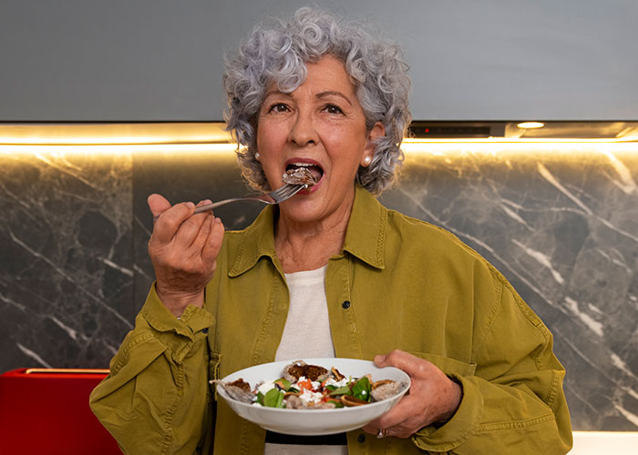 Older woman enjoying a meal while sharing things learned embarrassingly late in life with a warm kitchen background.