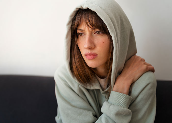Young woman in a hoodie sitting thoughtfully, representing people sharing things they've learned embarrassingly late in life.
