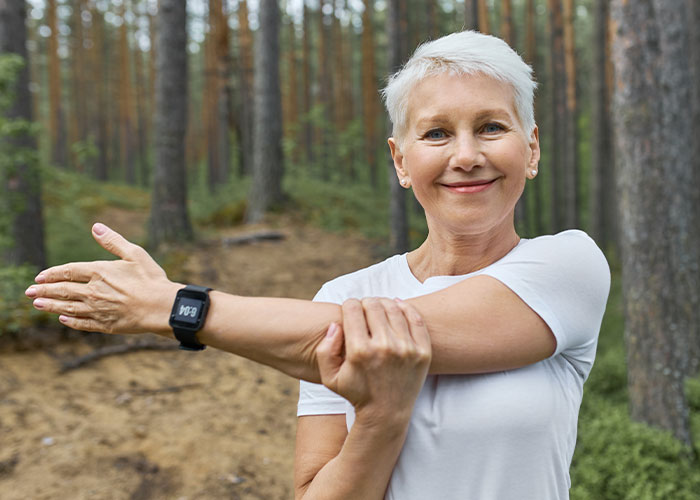 Smiling mature woman stretching arm outdoors in forest, symbolizing people sharing things learned late in life.