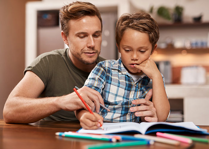Father helping son with homework, sharing knowledge and important life lessons in a home learning environment.