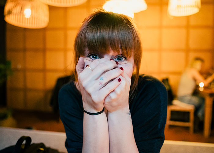 Young woman covering her face in embarrassment, sharing things learned embarrassingly late in life indoors.