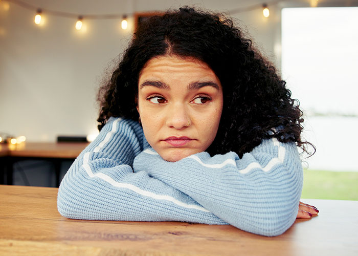 Young woman with curly hair resting on a table, reflecting on things people learned embarrassingly late in life.