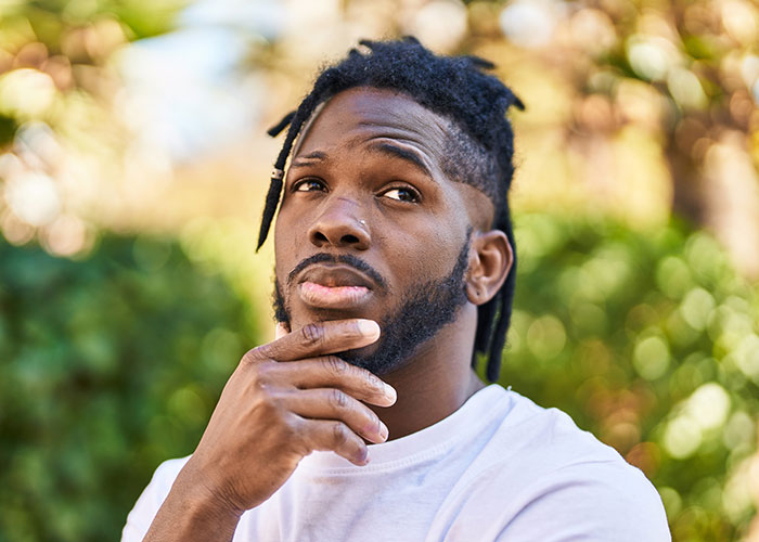 Young man with braided hair outdoors, thoughtfully reflecting on things learned embarrassingly late in life.