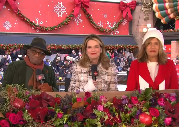 Three hosts seated with holiday decorations behind and festive flowers in front during Thanksgiving parade coverage. Three hosts seated with holiday decorations behind and festive flowers in front during Thanksgiving parade coverage.